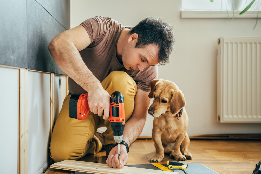 A man using a hand drill on wood while his dog watches