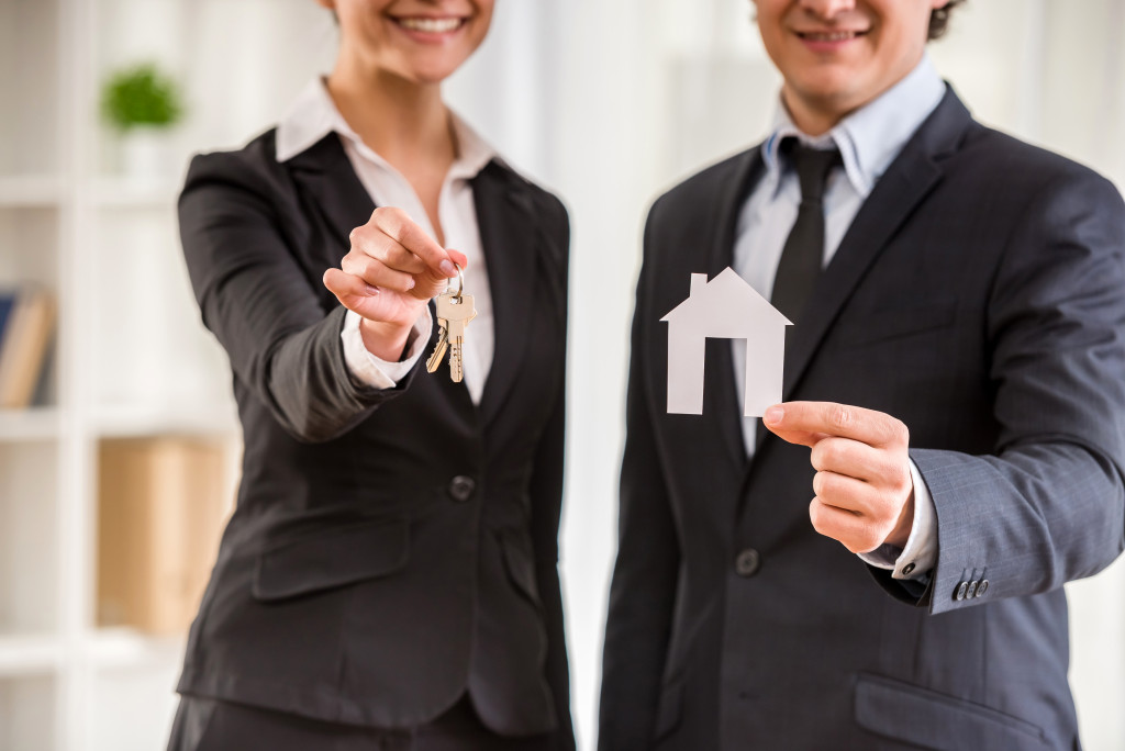 real estate agents; one holding the key the other holding a paper house